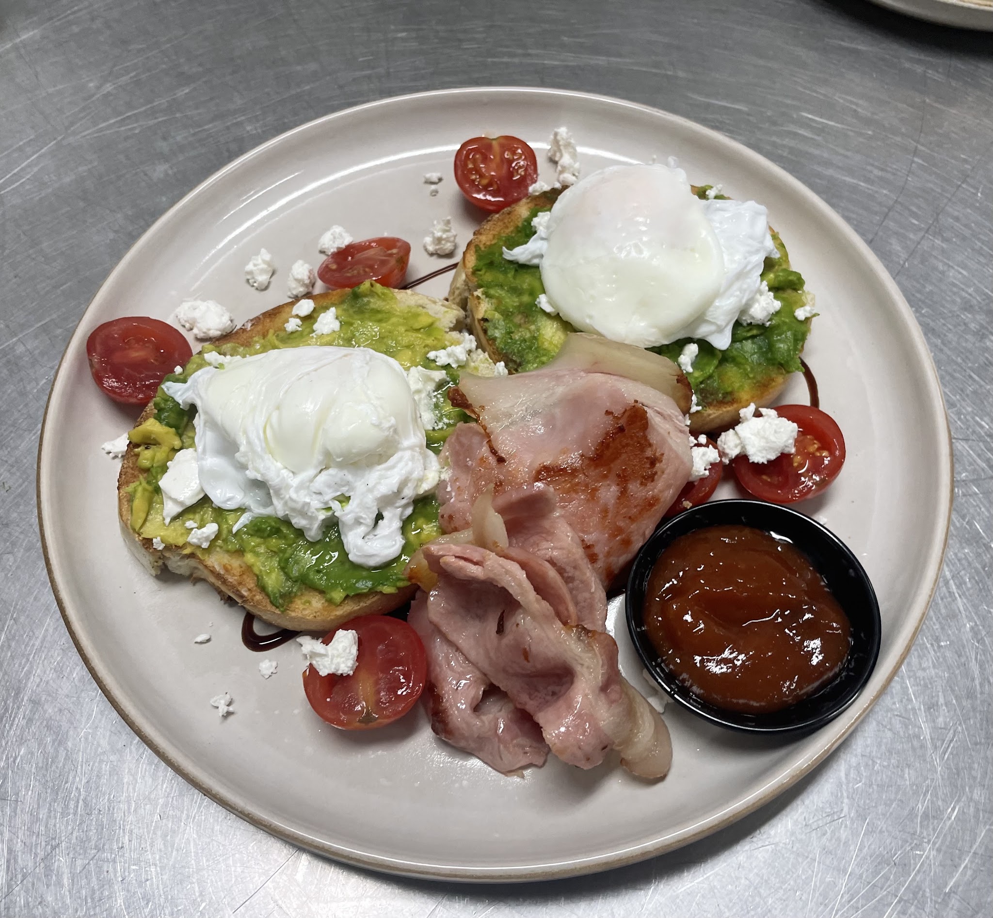 Smashed avocado on toasted sourdough with poached eggs, feta, bacon and cherry tomatoes