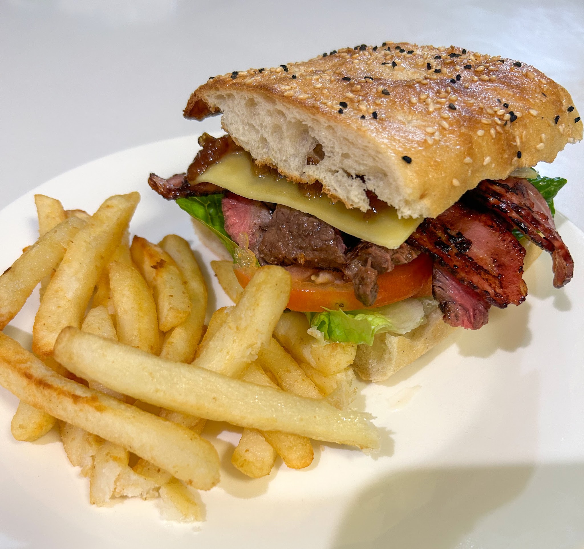 Steak sandwich on a black sesame Turkish roll with bacon, cheese, caramelised onion and chips